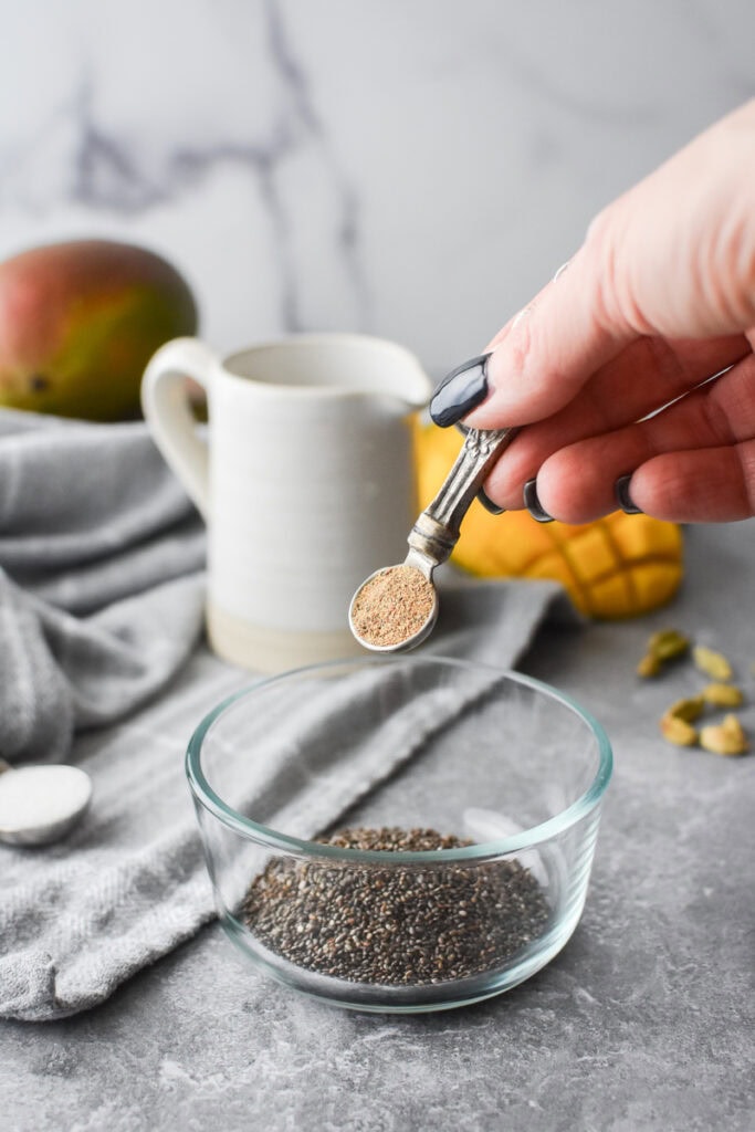 Adding cardamom to chia seeds in a glass bowl