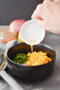 Adding vinegar to a bowl of mango, onion and cilantro