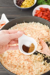 Adding spices to cauliflower rice in a pan