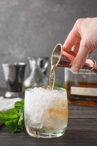 pouring bourbon into a glass of crushed ice