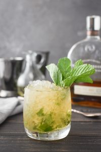 a mint julep with a bottle of bourbon and two julep cups