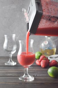 frozen strawberry daiquiri being poured from a blender into a glass.