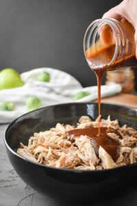 Adding barbecue sauce to a bowl of shredded chicken