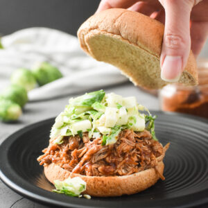 putting a bun top on top of a shredded apple barbecue chicken sandwich