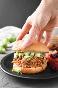 putting the top bun on a shredded apple barbecue chicken sandwich
