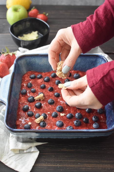 adding the oat dough to the top of a pan of red, white and blue berry crumb bars