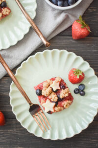 a green plates with a red white and blue berry crumb bar and a copper fork