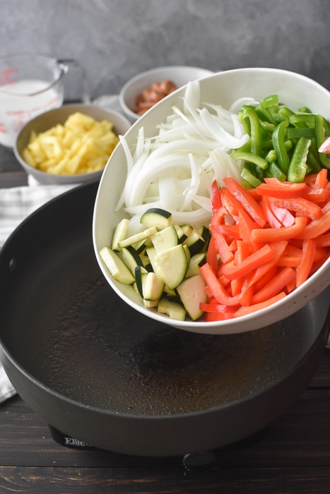 Adding vegetables to a non-stick pan.