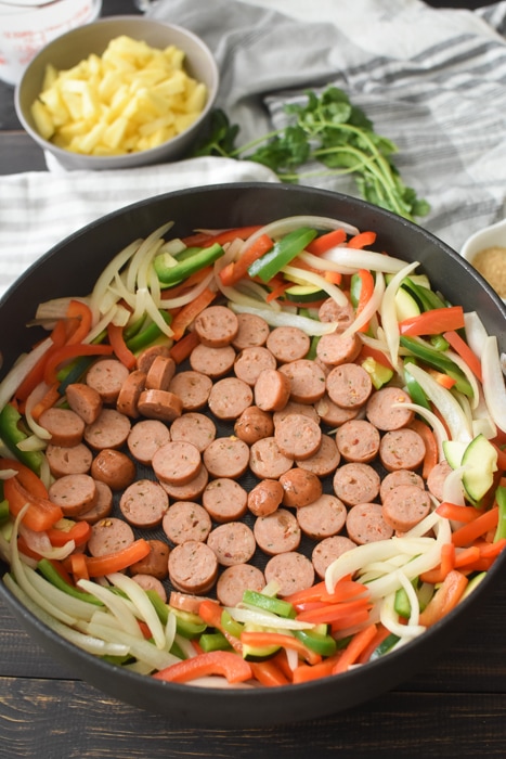 A pan that has cooked veggies that have been pushed to the outside of the pan, with sliced sausage in the center of the pan.
