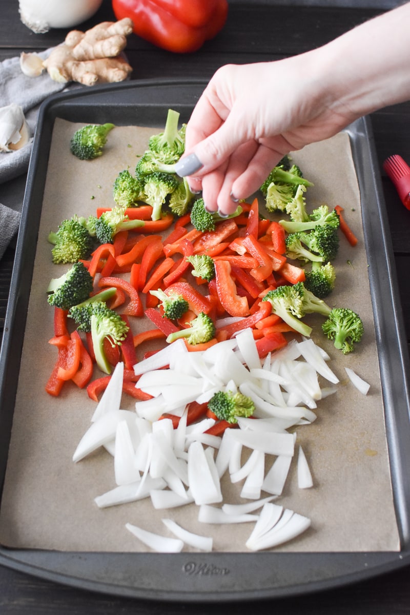 Sprinkling salt over a sheet pan full of vegetables.