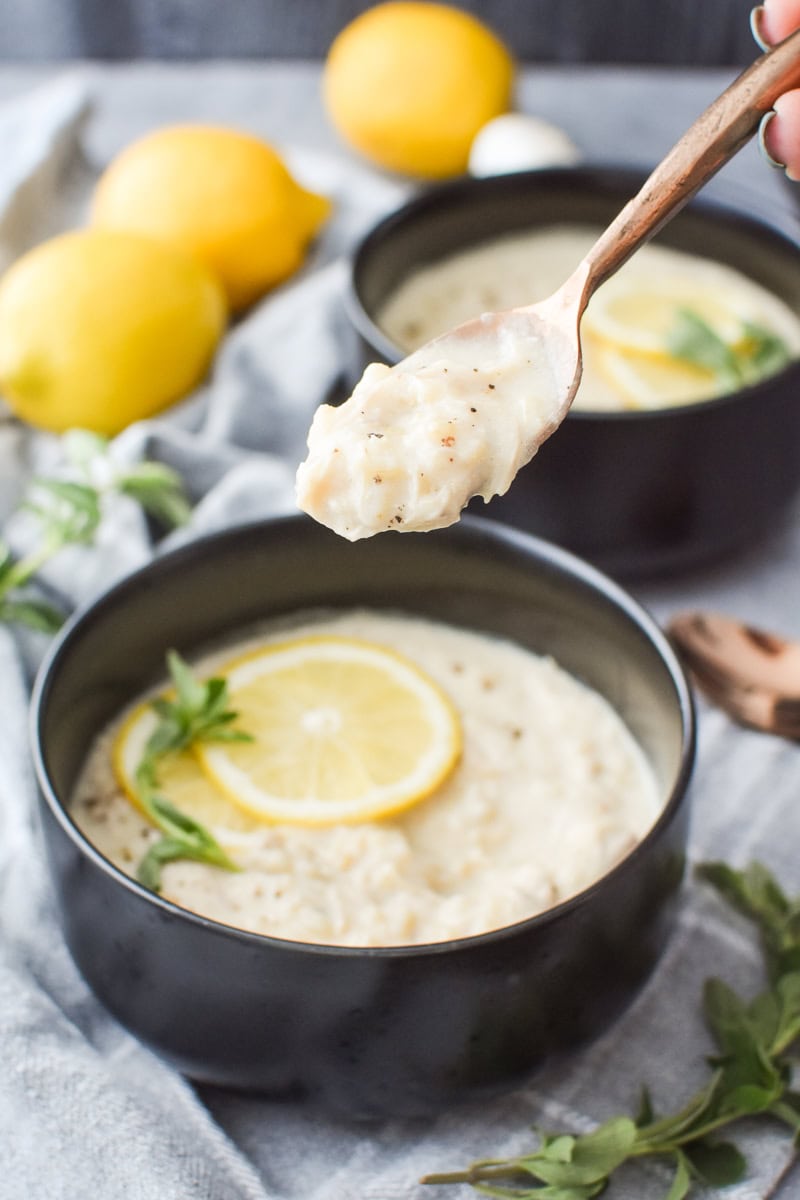 A spoonful of avgolemono soup with a bowl of the soup in the background.