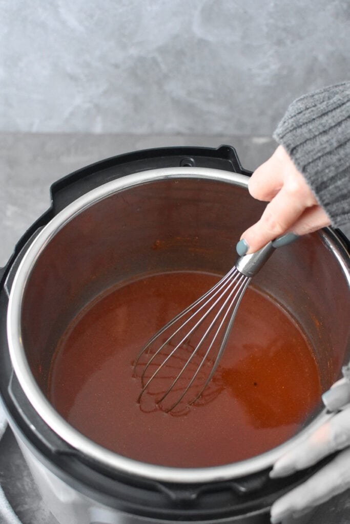 Whisking together apple cider bbq sauce in an Instant Pot.