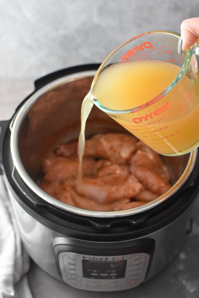 Adding broth to an Instant Pot full of seasoned chicken.