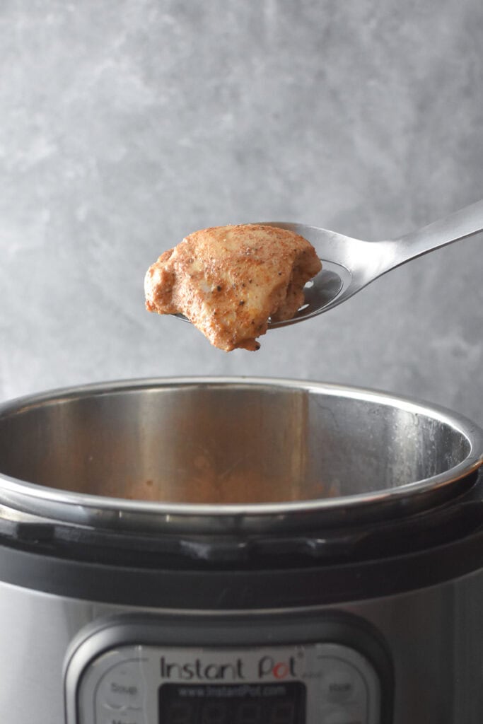 A cooked chicken thigh on a slotted spoon above an Instant Pot.