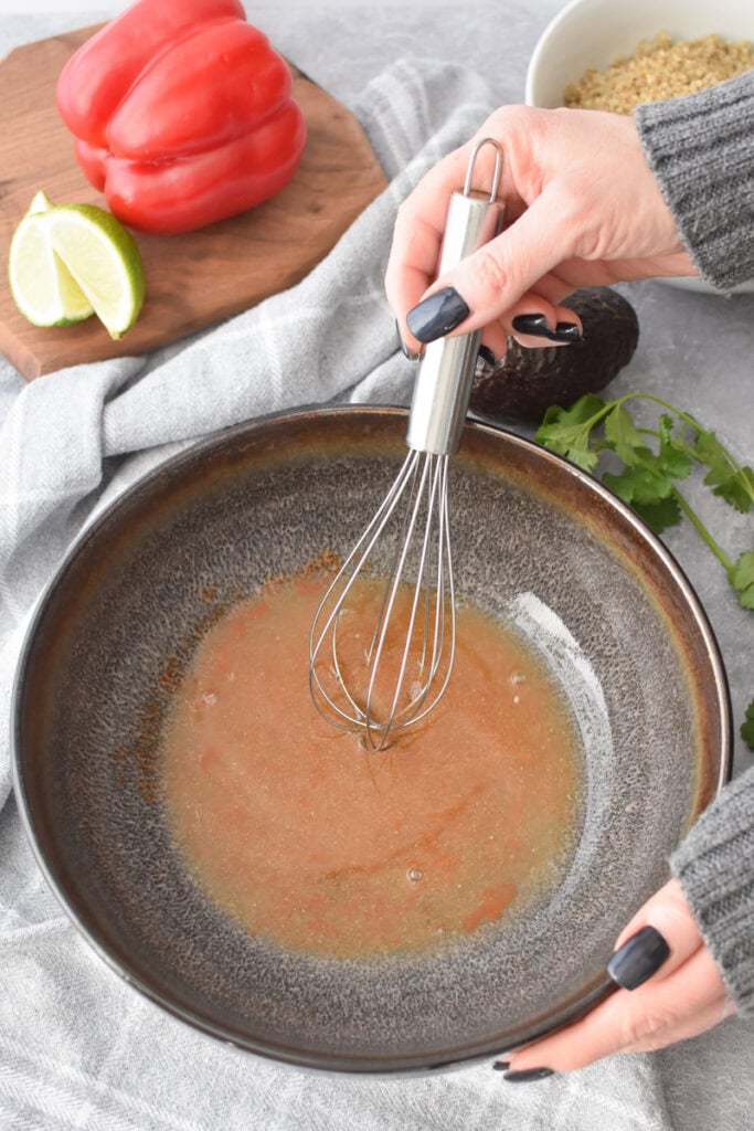 Whisking dressing in a large, brown bowl.