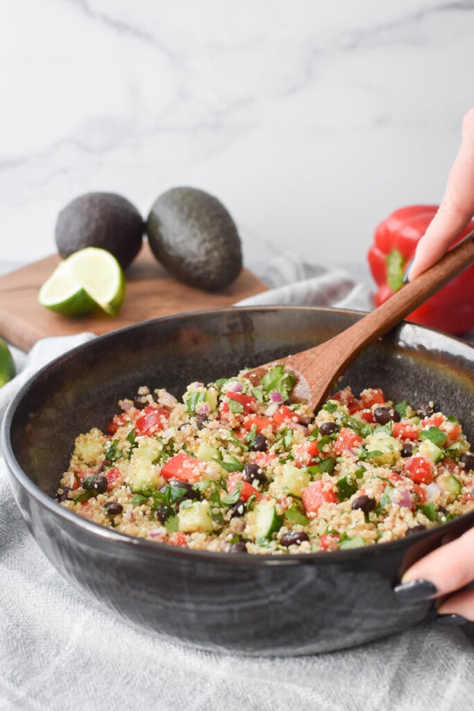 Mixing together all of the ingredients for Cilantro Lime Quinoa Salad in a large brown bowl.