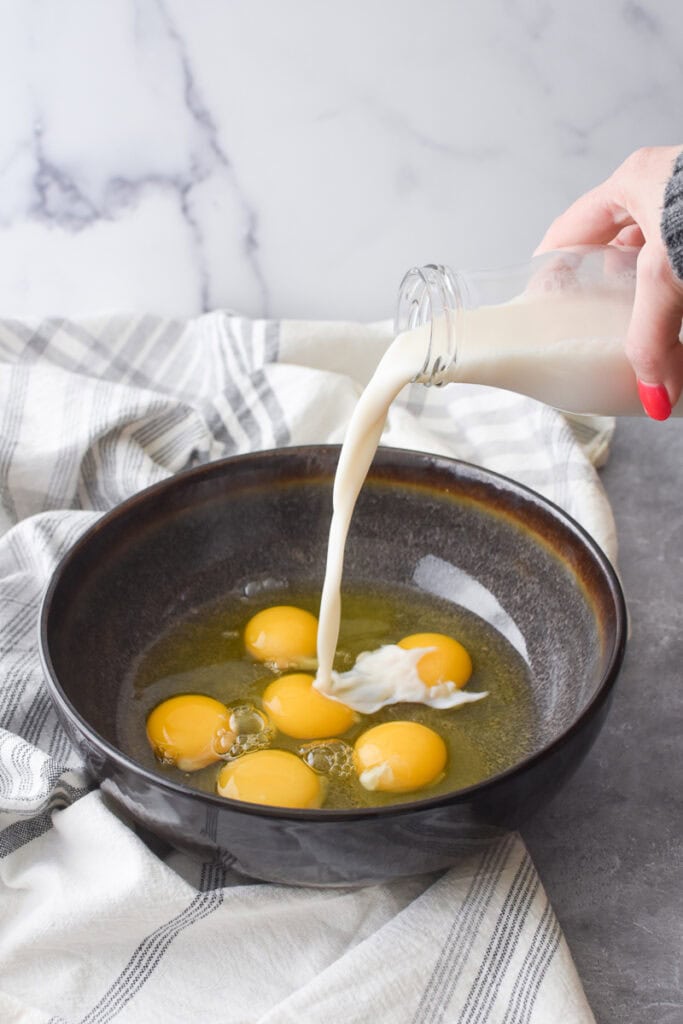 Adding almond milk to a large, brown bowl full of eggs.