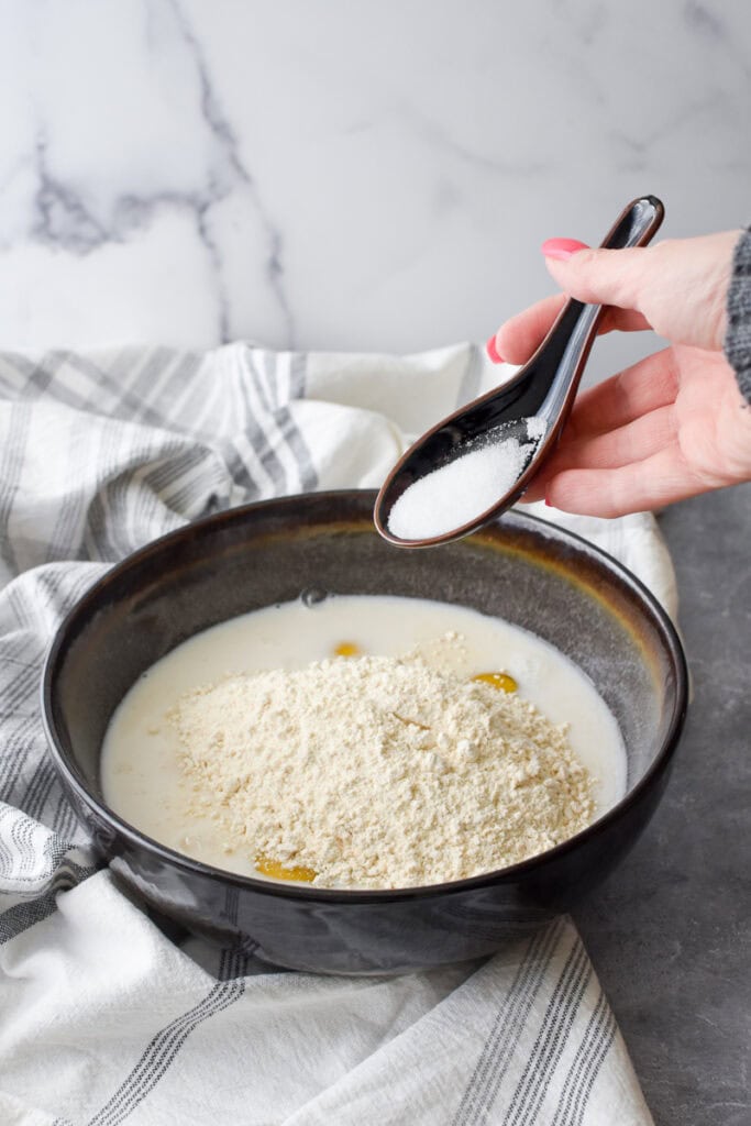 Adding salt to the ingredients for Whole Wheat German Pancake in a large brown bowl.