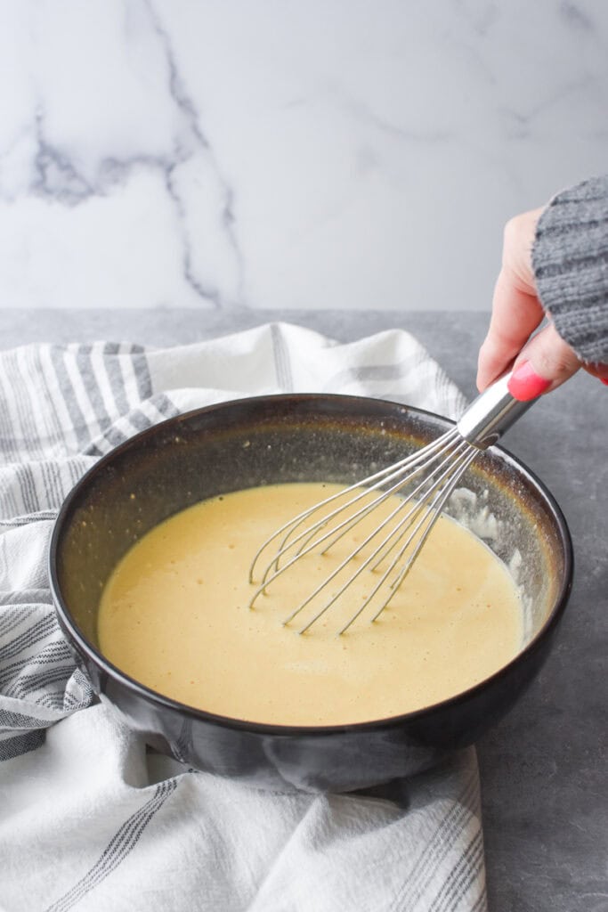 Whisking the ingredients for Whole Wheat German Pancake in a large brown bowl.