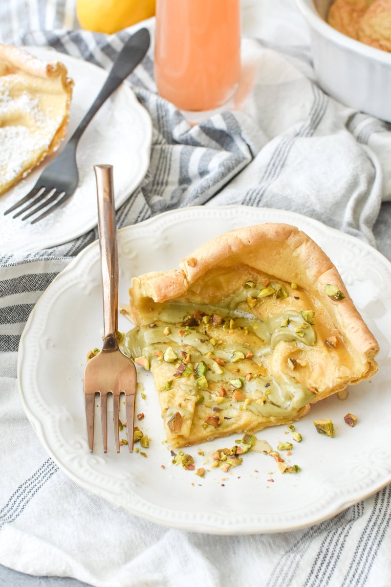 A piece of Whole Wheat German Pancake drizzled with pistachio nut butter, chopped pistachios, and honey, on a white plate.