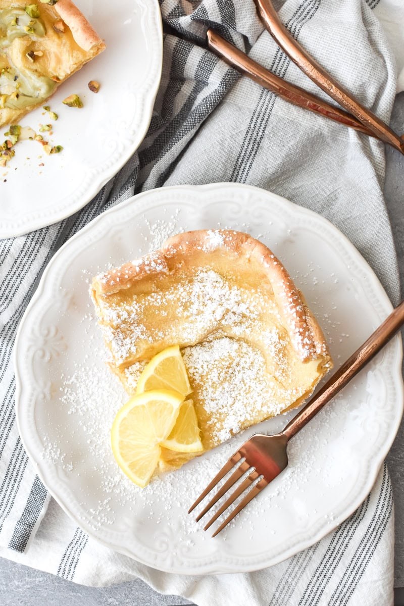 A piece of Whole Wheat German Pancake with lemon slices, covered in powdered sugar on a white plate.